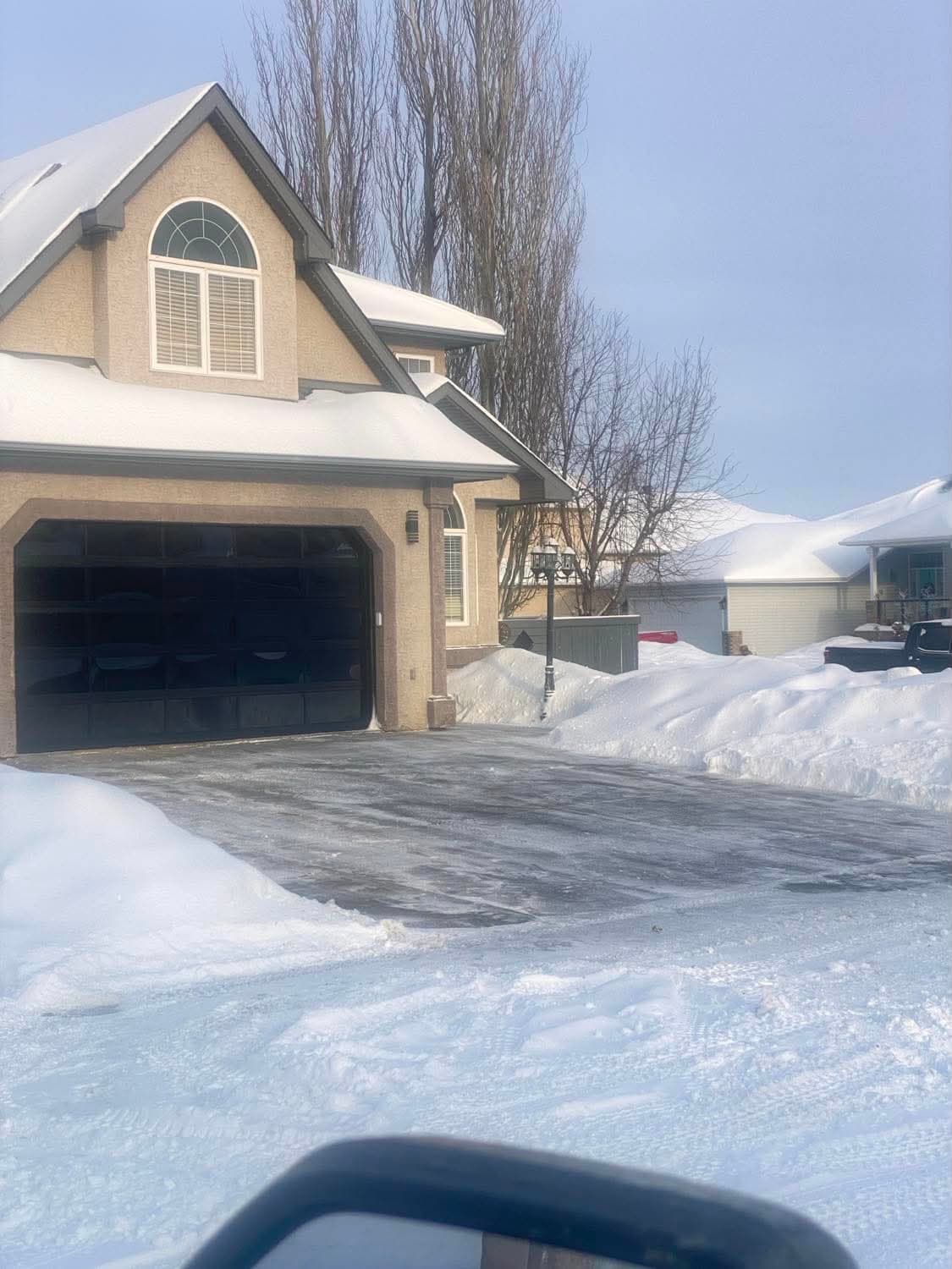 A residential driveway cleared down to the pavement between deep snowbanks after a snowfall