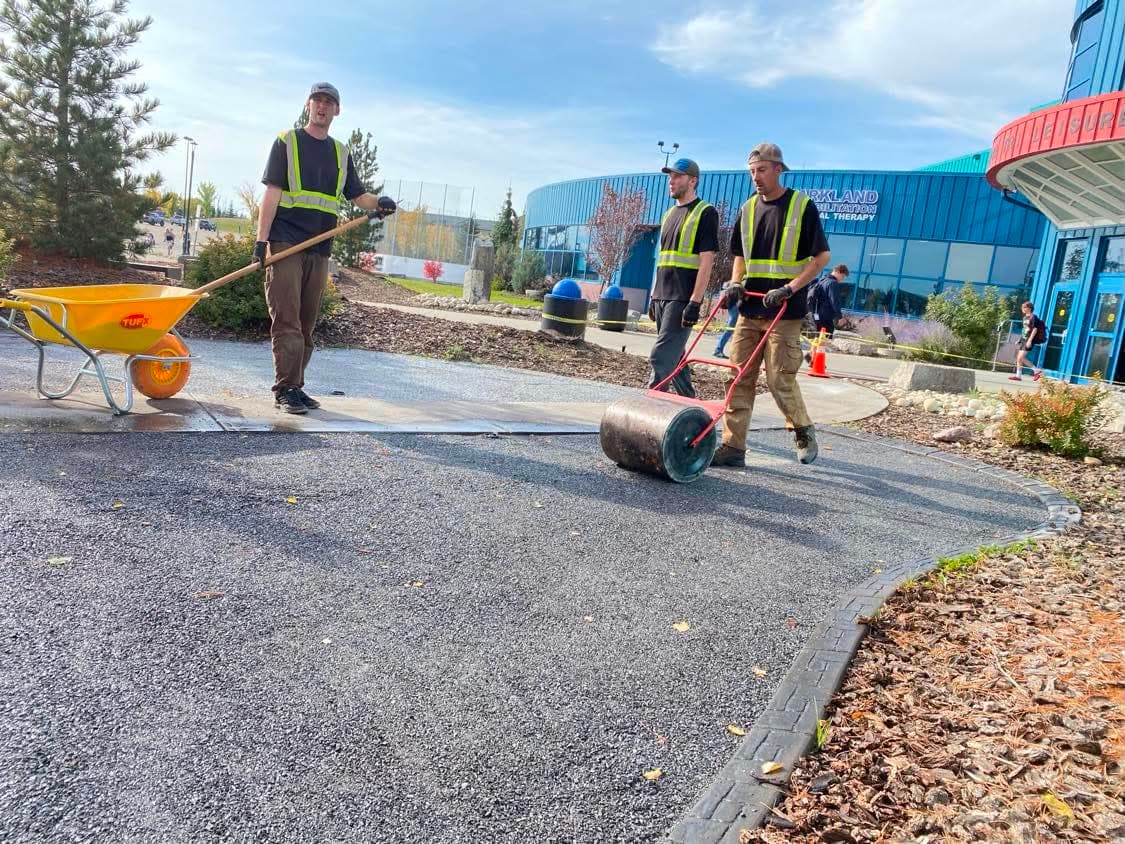 Three Phoenix Landscaping crew members in high-visibility vests working together on a commercial site